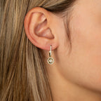 תקריב של אוזן של אישה עונדת עגיל חישוק מזהב עם אבן חן עגולה.