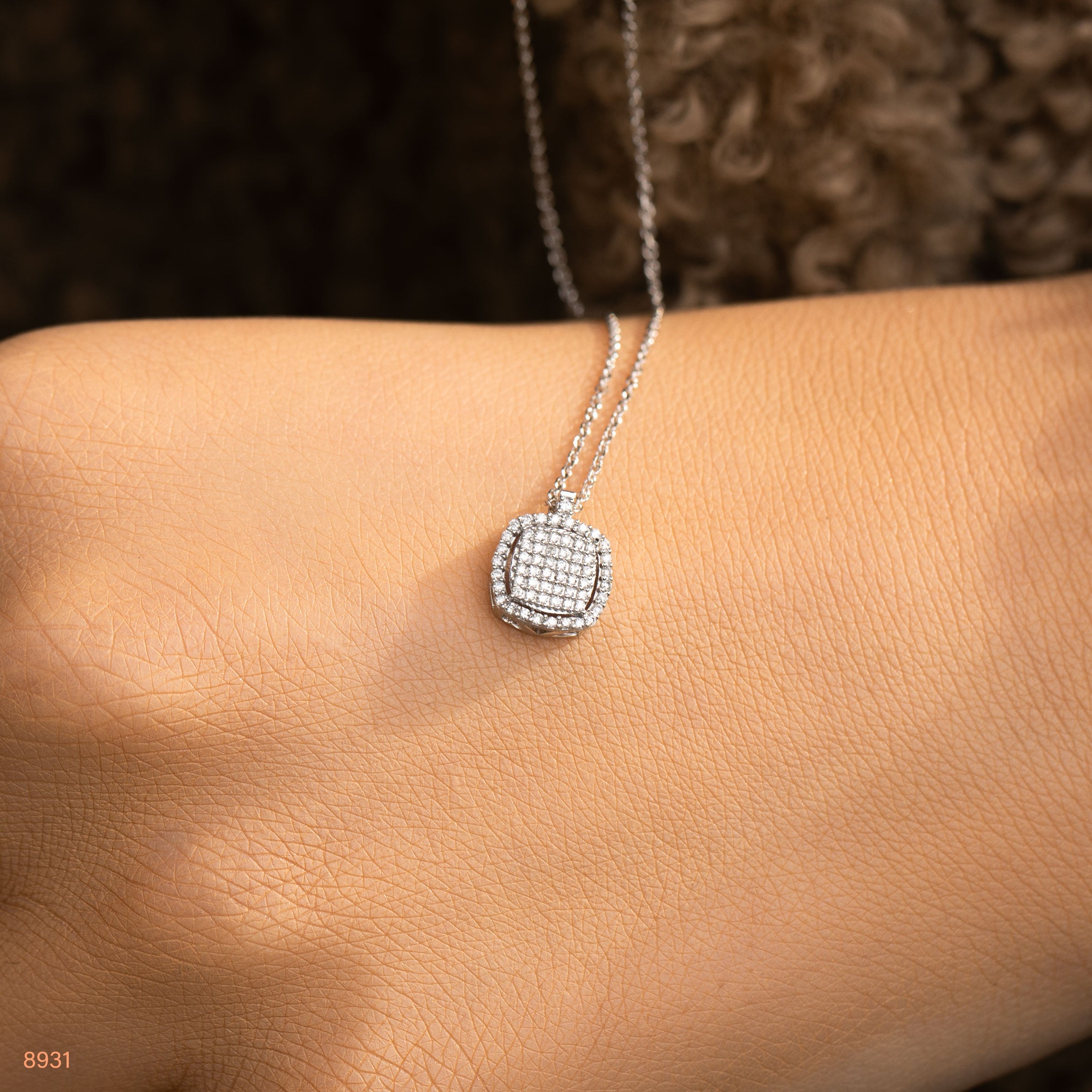 תקריב של שרשרת כסף עם תליונית מרובעת מונחת על פרק כף היד של דוגמנית