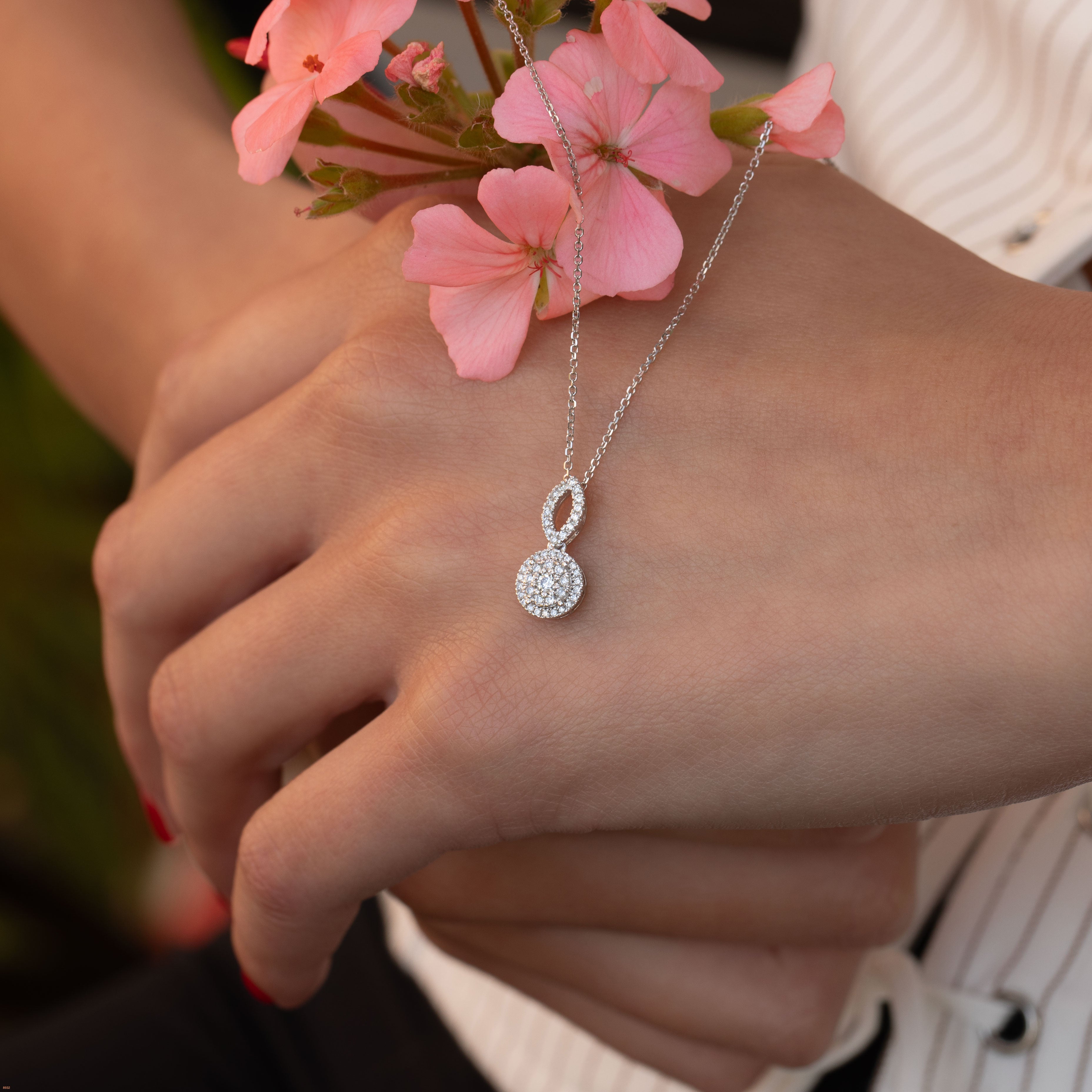 תקריב של יד עונדת שרשרת עם תליונית יהלום, עם פרחים ורודים ברקע.