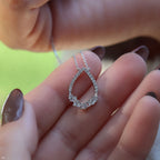 תקריב של יד מחזיקה בשרשרת עם תליון טיפה כסף עם פרטים מורכבים כמו יהלומים.