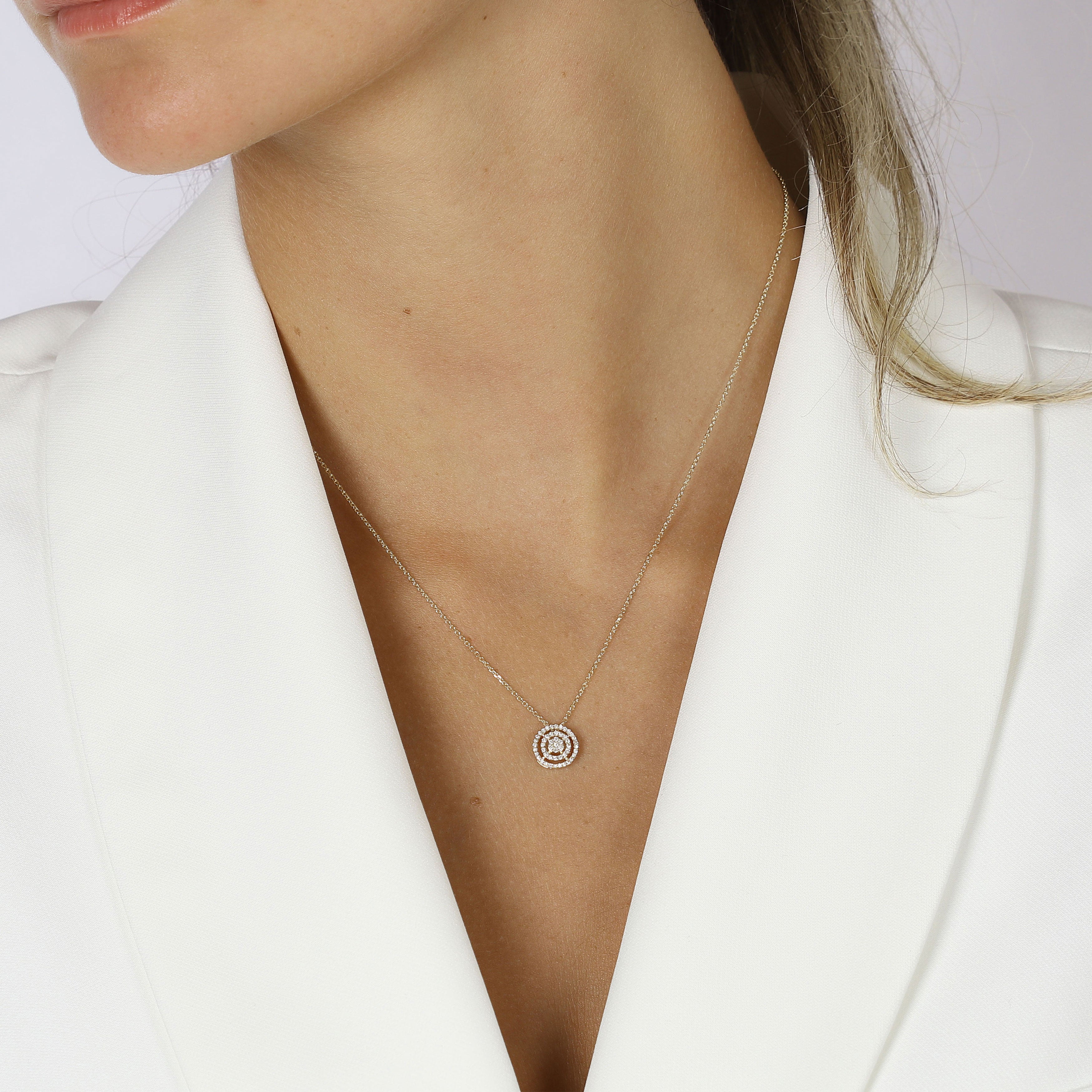 תקריב של אישה לובשת שרשרת כסף עדינה עם תליון עגלגל, לבושה בז'קט לבן.