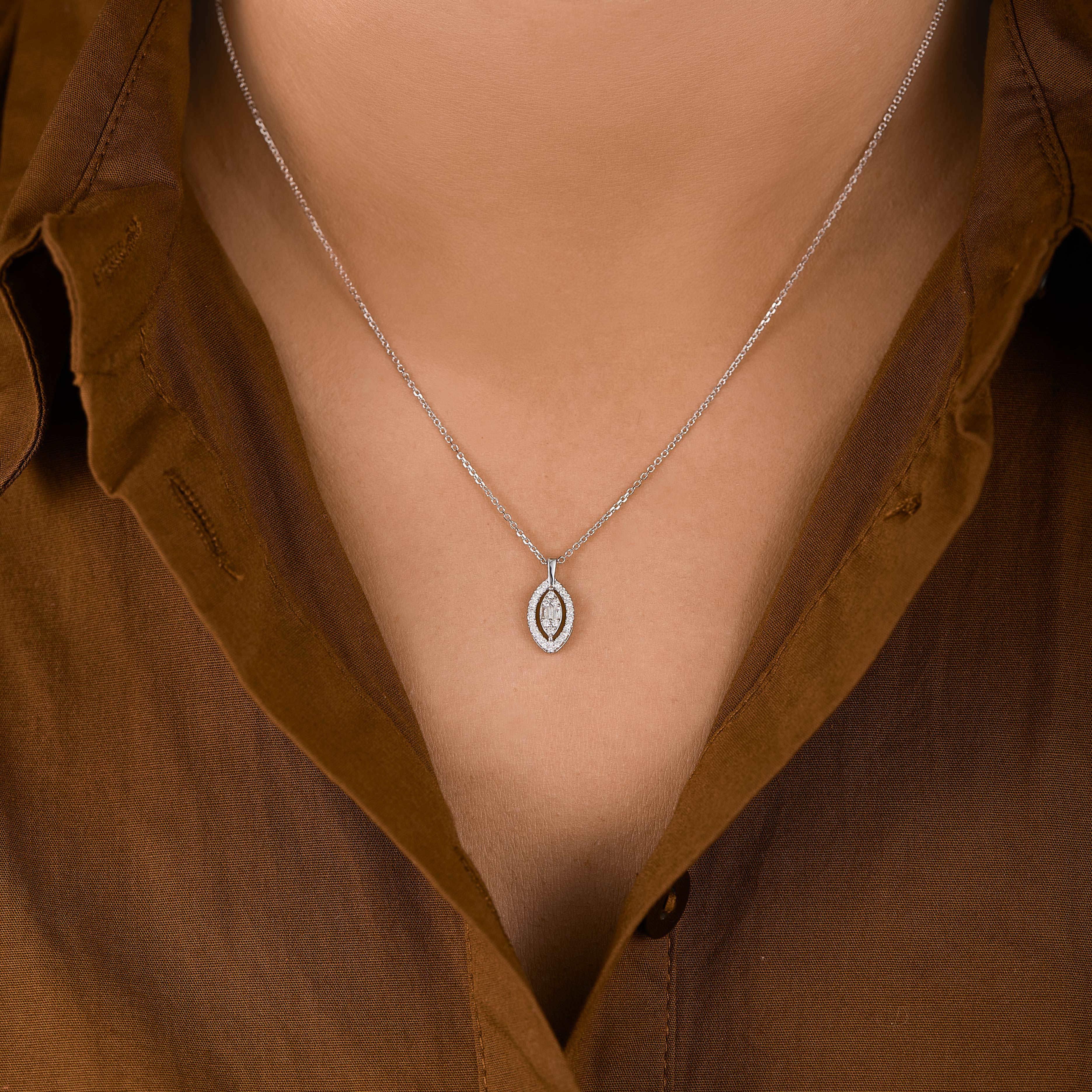 תקריב של שרשרת כסף עם תליון טיפה, שנלבשת על אדם עם חולצה חומה.