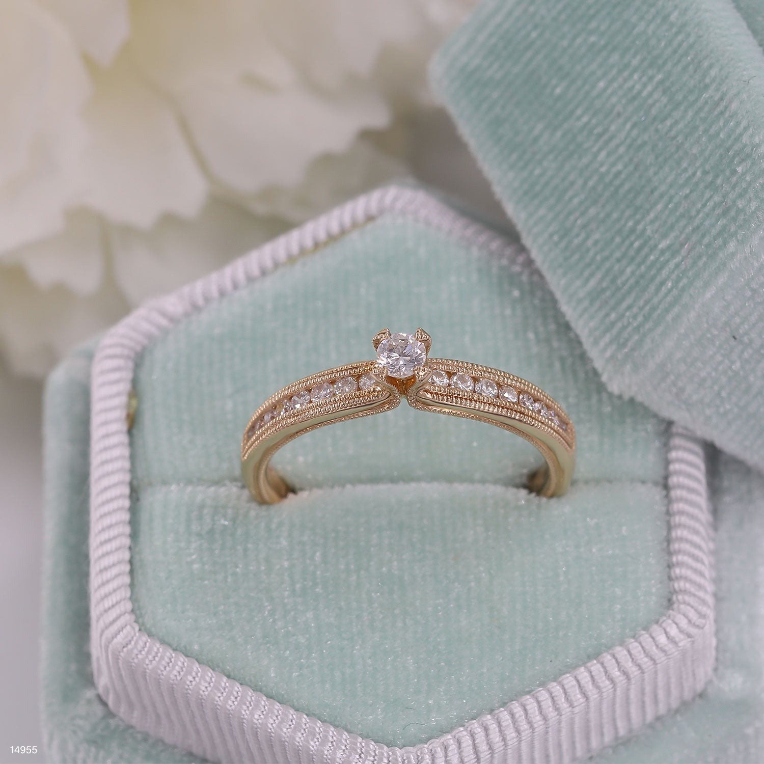 טבעת זהב עם יהלום מרכזי ואבנים קטנות יותר, מוצגת בתוך קופסה רכה של קטיפה כחולה.