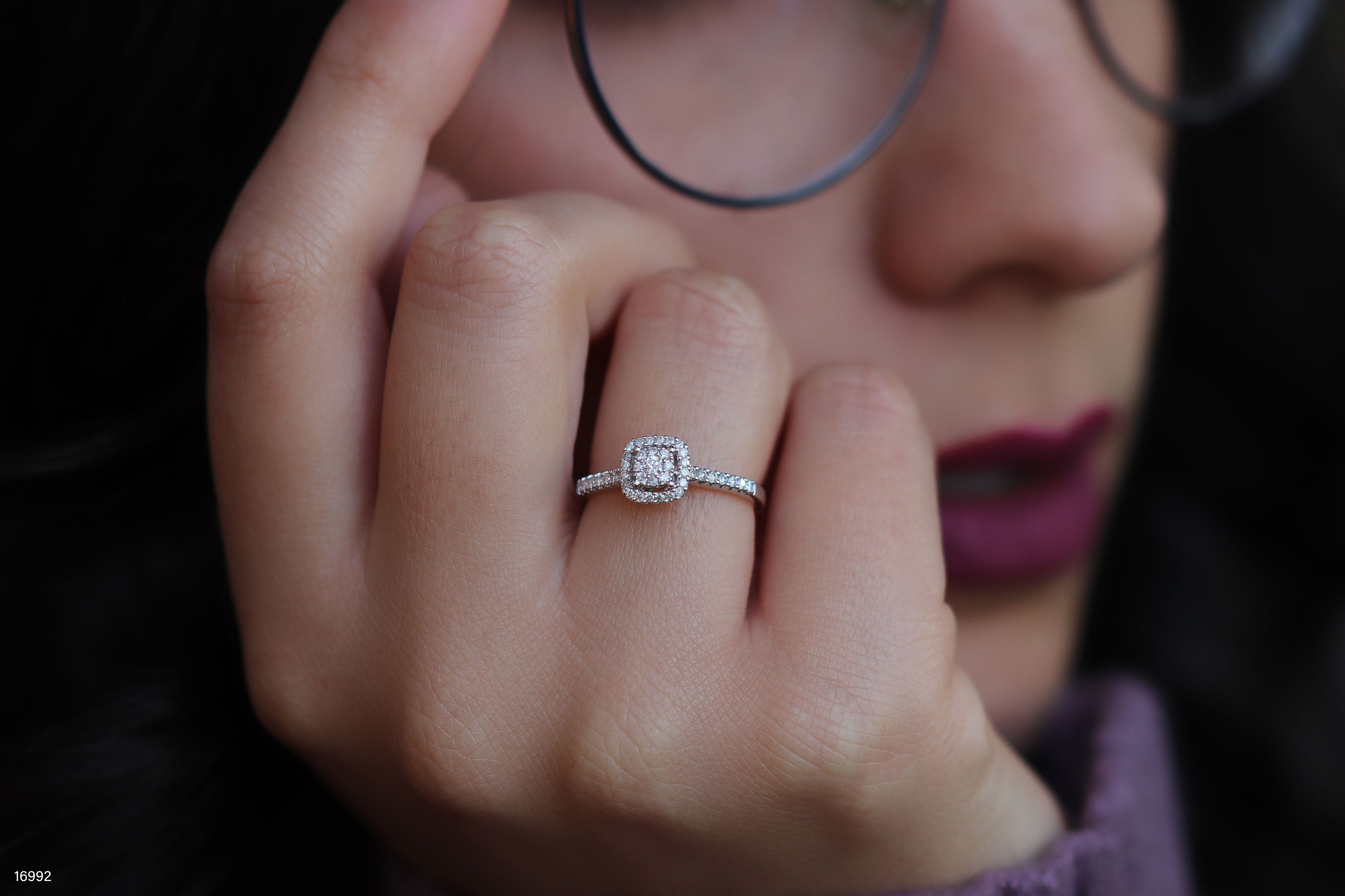 תקריב של יד עם טבעת יהלום, מראה אישה עם משקפיים ברקע.