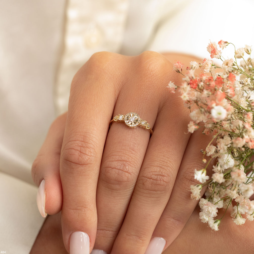 יד של אדם מעוטרת בטבעת זהב עדינה, מחזיקה בזוג פרחים קטנים.