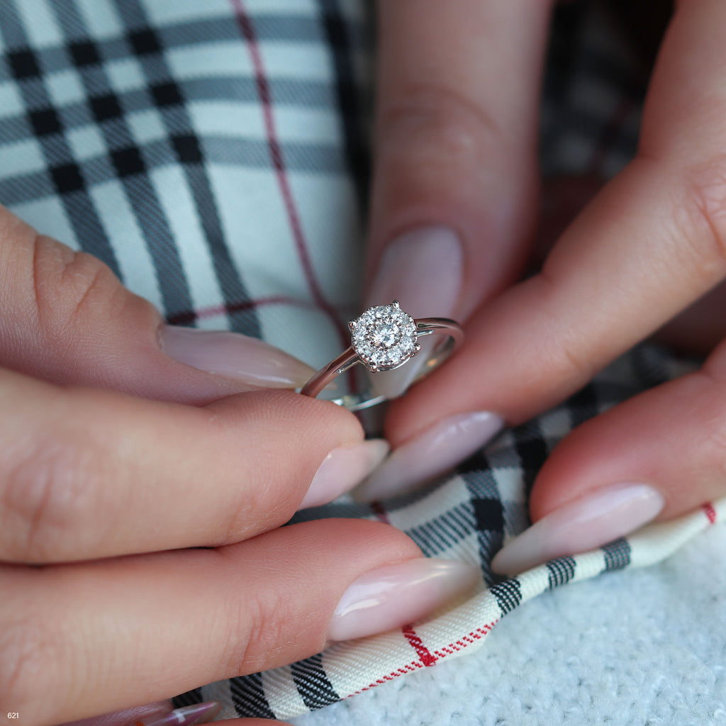 תקריב של יד מחזיקה בטבעת אירוסין מבריקה על רקע בד עם דוגמה.