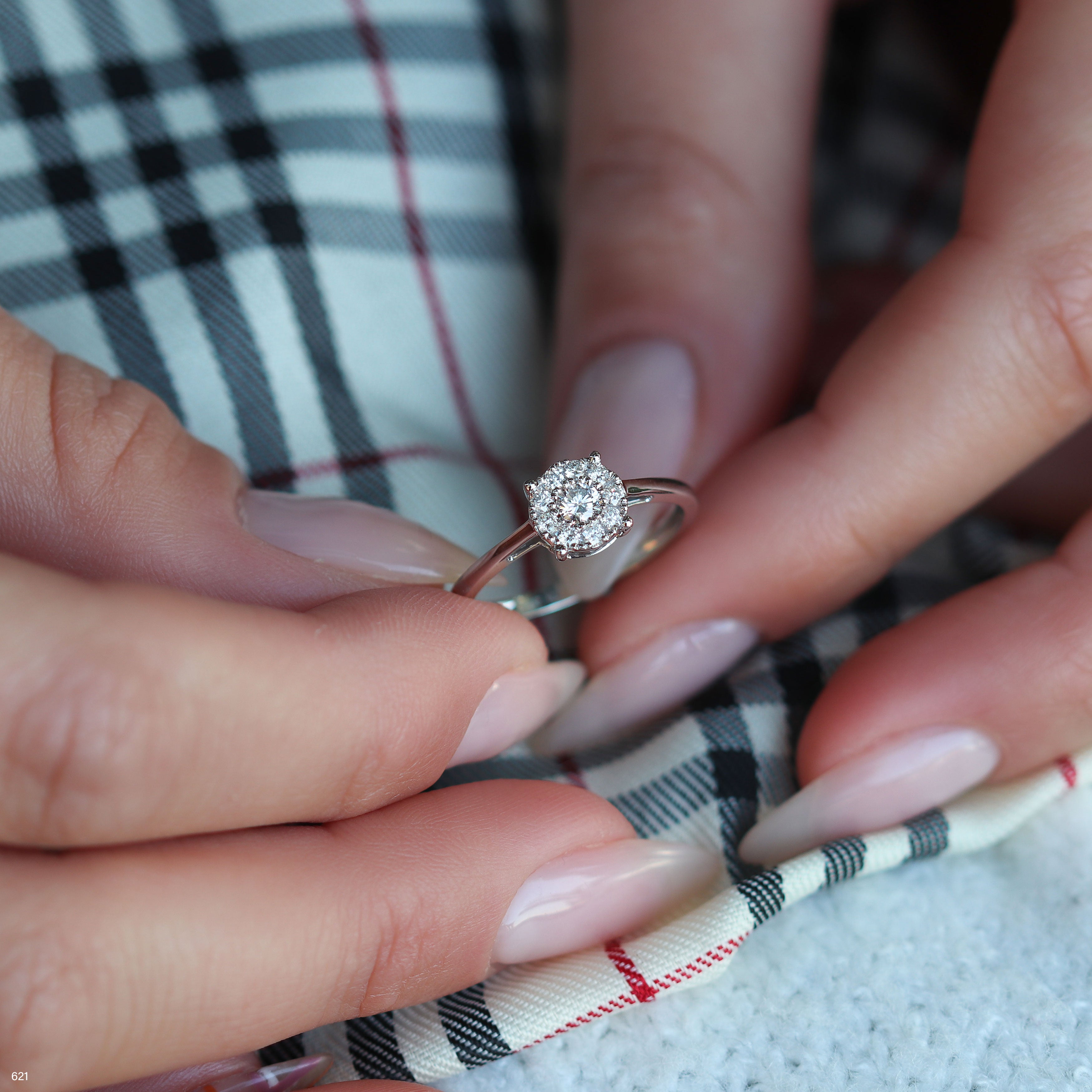 תקריב של יד מחזיקה בטבעת אירוסין מבריקה על רקע בד עם דוגמה.