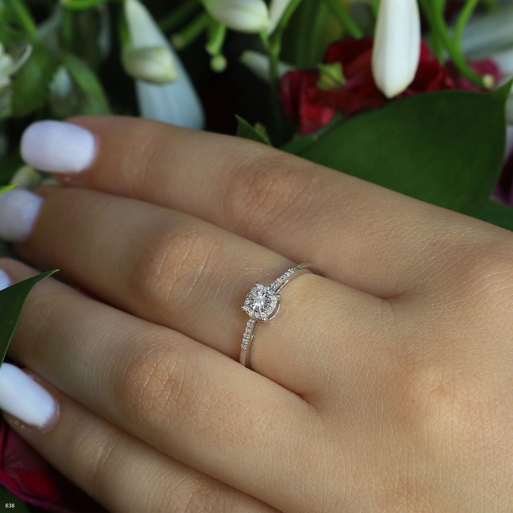 תקריב של יד עונדת טבעת כסף עדינה עם אבן חן עגולה, מוקפת בפרחים.