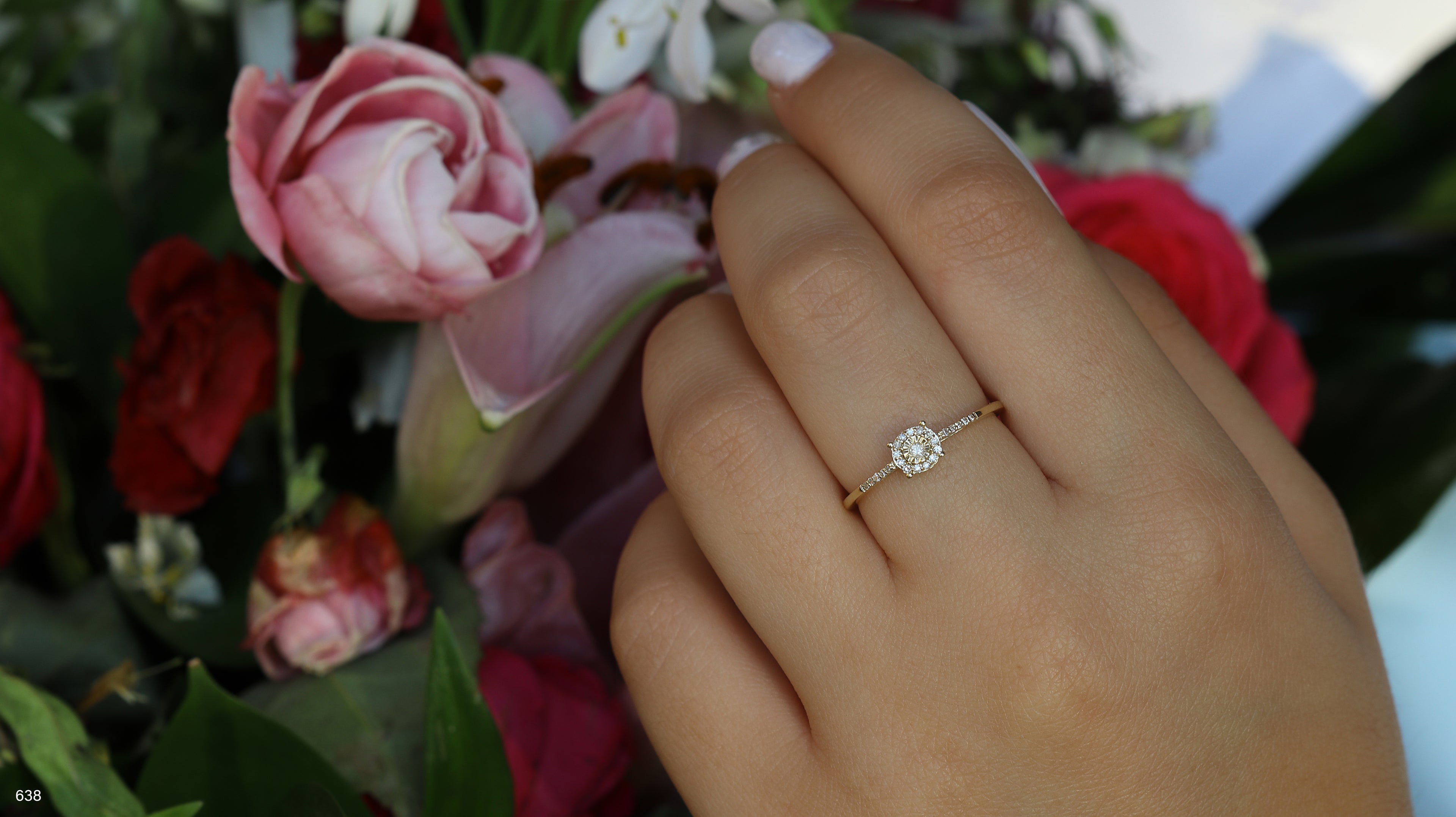 יד לובשת טבעת עדינה, מוקפת בפרחים צבעוניים.