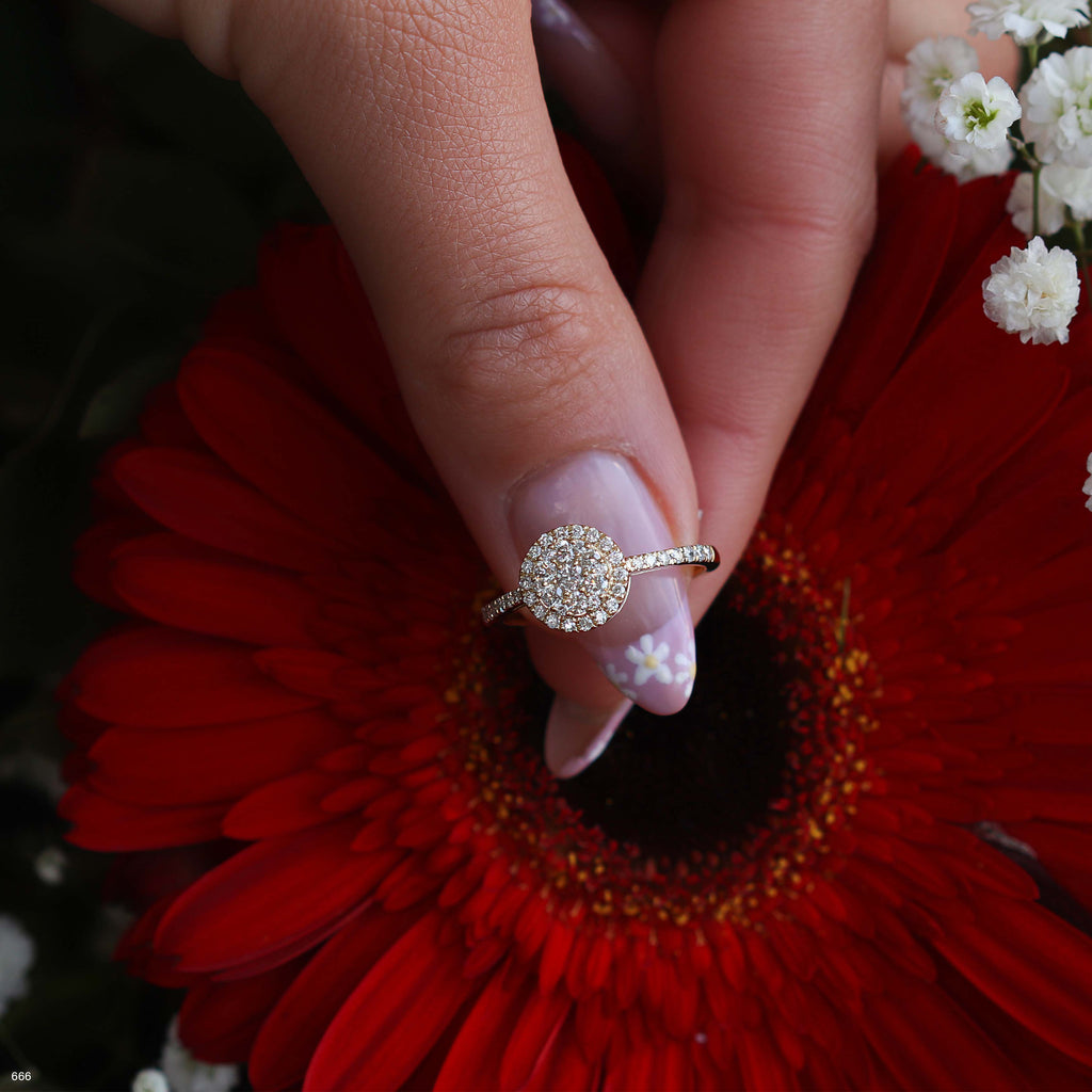 יד מחזיקה בטבעת זהב עם דיאמנט עגול מקדימה של פרח אדום.