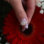 יד מחזיקה בטבעת זהב עם דיאמנט עגול מקדימה של פרח אדום.