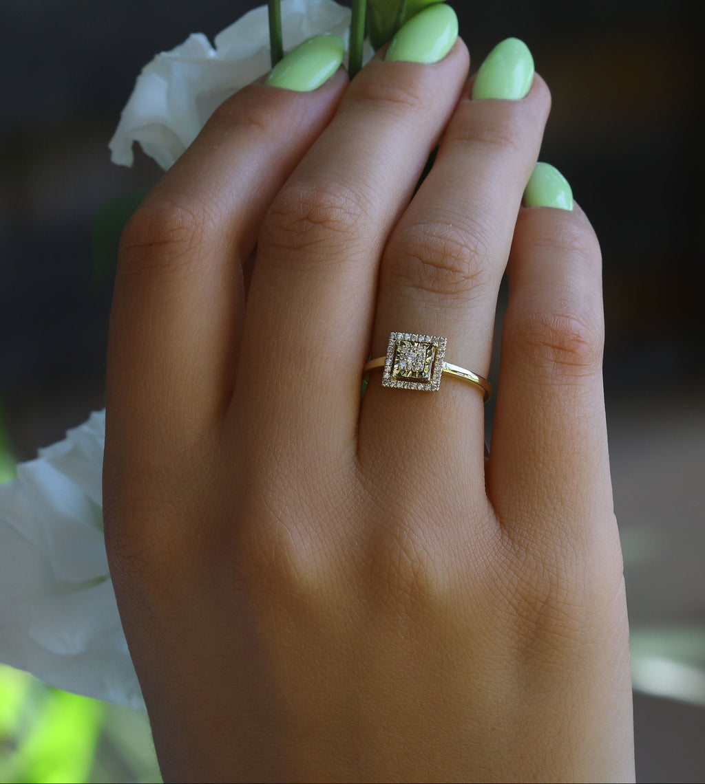 תקריב של יד עם ציפורניים ירוקות בהירות שעונדת טבעת אירוסין עם יהלום מרובע.