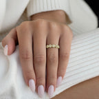 תקריב של יד עונדת טבעת זהב עם אבני חן, מונחת על בד לבן עם מרקם.