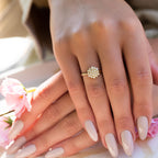 תקריב של יד עם טבעת פרחונית וציפורניים מטופחות, מונחת על שולחן עם פרחים ורודים.