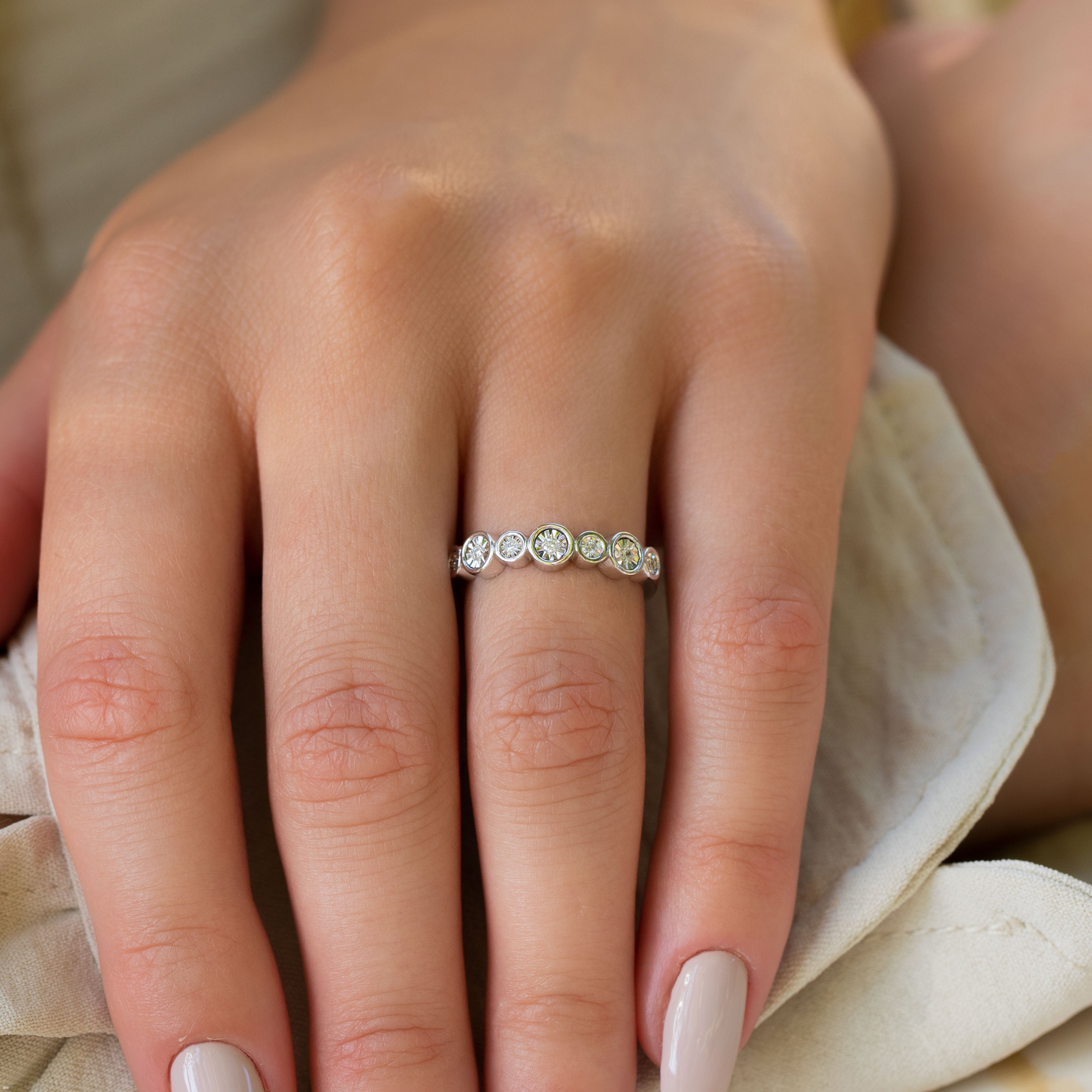 תקריב של יד עונדת טבעת כסף עדינה עם מספר אבני חן קטנות.