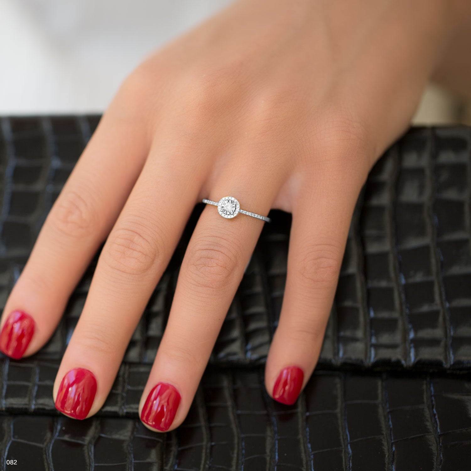 תקריב של יד אישה עם טבעת כסף ומניקור אדום על משטח שחור עם מרקם.