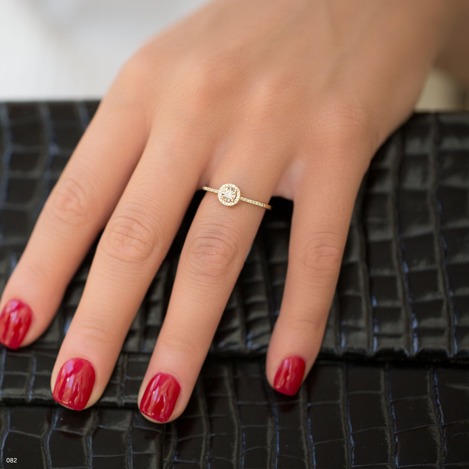 תקריב של יד עם טבעת זהב עם אבן חן קטנה, מונחת על משטח שחור עם מרקם.