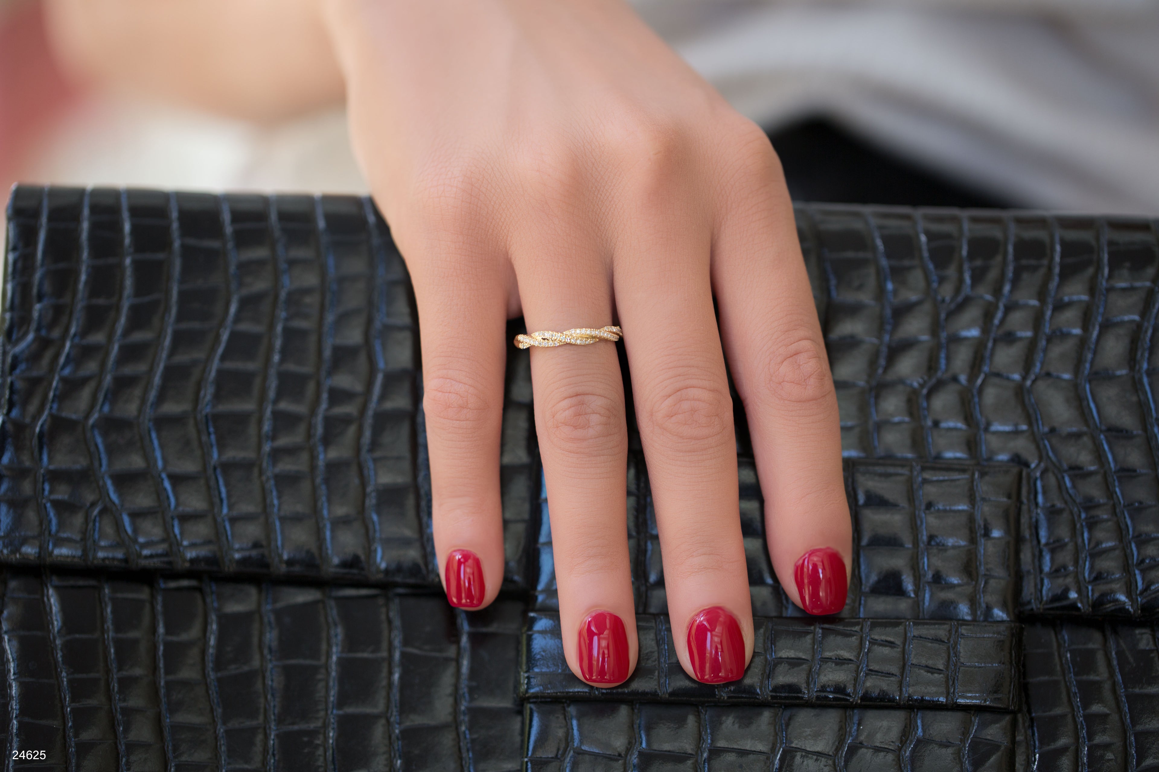 יד עם לק אדום מונחת על תיק יד עם הדפס קрокו שחור.