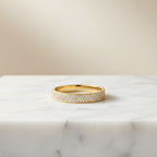 טבעת זהב מעוטרת ביהלומים קטנים על משטח שיש.