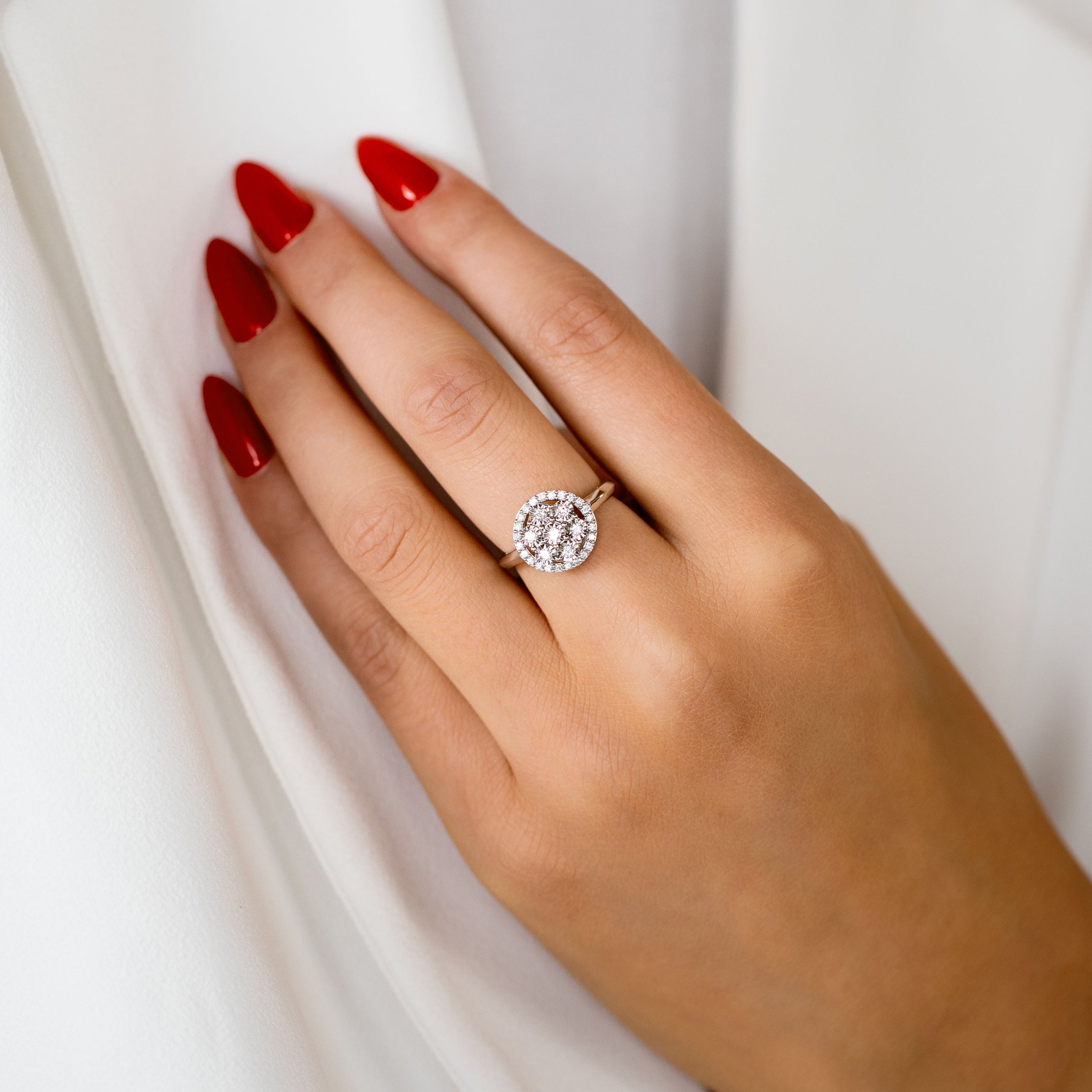 תקריב של יד עם ציפורניים אדומות שעונדת טבעת מנצנצת על רקע לבן.