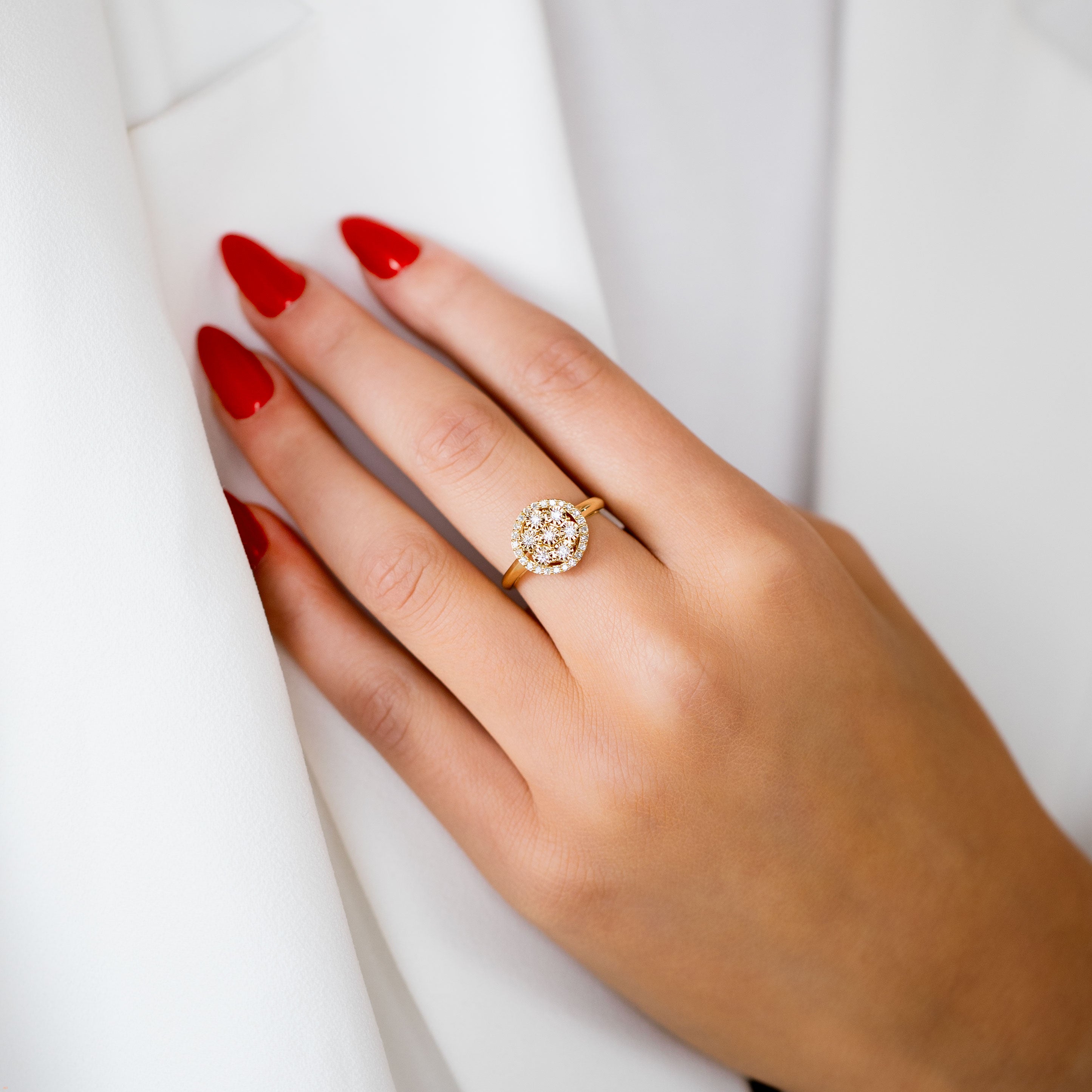 תקריב של יד עונדת טבעת זהב בעיצוב פרחוני, מציגה ציפורניים אדומות ארוכות על רקע לבן.