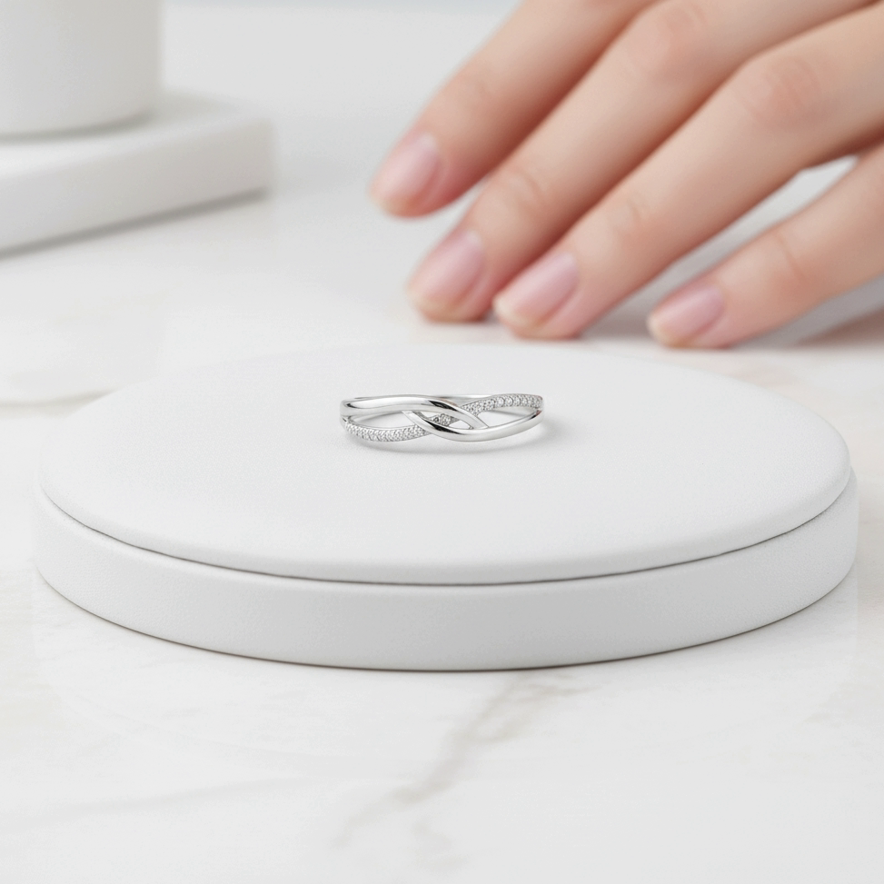 טבעת כסף עם עיצוב מסולסל מוצגת על בסיס עגול לבן, עם יד שמתקרבת אליה בעדינות.