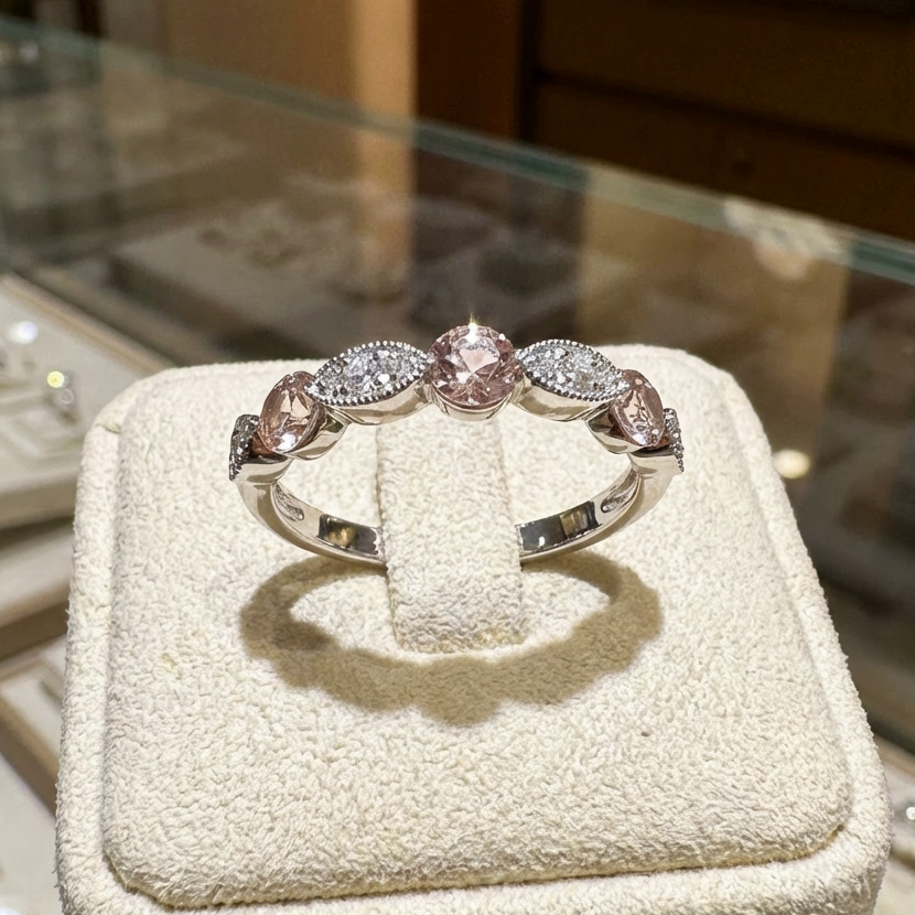 טבעת כסף עם אבני חן ורודות וברורות מוצגת על בסיס עם מרקם.