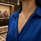 תקריב של אישה לובשת חולצה כחולה ושרשרת זהב עם תליונית, על רקע תצוגות תכשיטים.